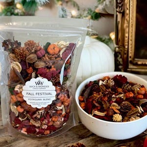 May include: A clear bag and a white bowl filled with Fall Festival Potpourri Blend. The potpourri includes small pumpkins, pinecones, and dried flowers in shades of orange, red, and brown. The bag has a label that says "Wick & Wonder Candle Company".