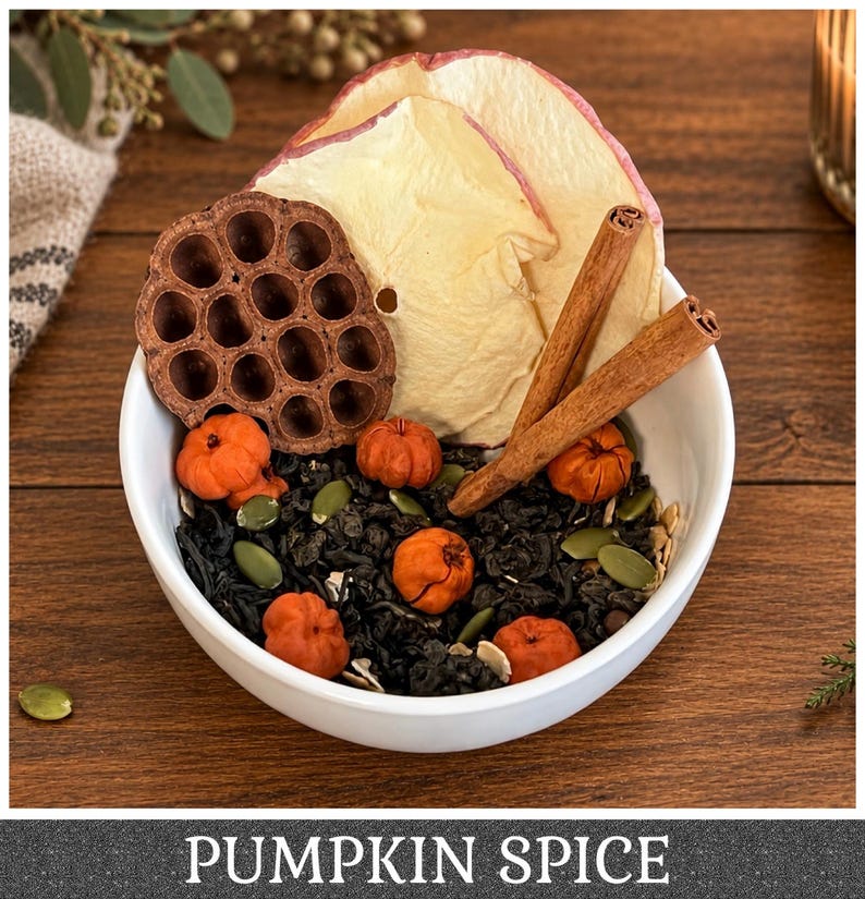 May include: A white bowl filled with a loose leaf tea blend containing small orange pumpkin-shaped pieces, green pumpkin seeds, dried apple slices, a brown lotus seed pod, and two cinnamon sticks, with the text PUMPKIN SPICE at the bottom.