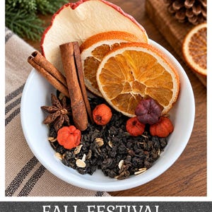 May include: A white bowl containing a blend of dark loose-leaf tea, dried apple slices, orange slices, cinnamon sticks, star anise, and small red berries. The text FALL FESTIVAL is printed at the bottom of the image in white capital letters.