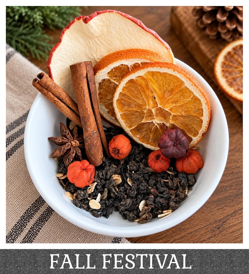 May include: A white bowl containing a blend of dark loose-leaf tea, dried apple slices, orange slices, cinnamon sticks, star anise, and small red berries. The text FALL FESTIVAL is printed at the bottom of the image in white capital letters.