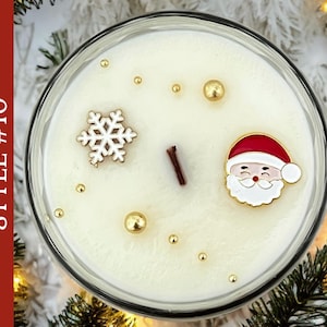 May include: A round candle in a glass container with white wax, featuring a central wooden wick, a white snowflake charm, a Santa Claus face charm, and scattered gold-colored spherical beads. The text STYLE #10 is visible on the left side.