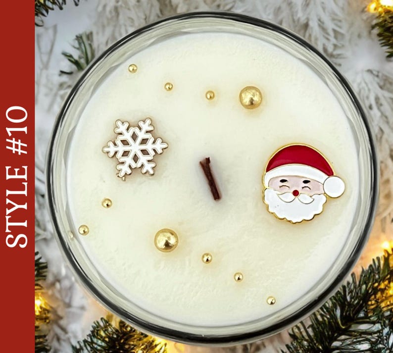 May include: A round candle in a glass container with white wax, featuring a central wooden wick, a white snowflake charm, a Santa Claus face charm, and scattered gold-colored spherical beads. The text STYLE #10 is visible on the left side.