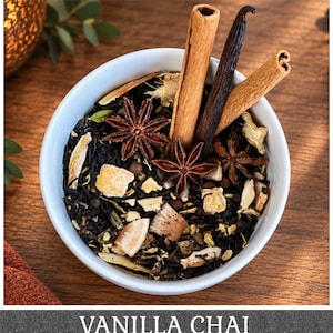 May include: A white bowl filled with loose leaf tea, featuring dark tea leaves, star anise, cinnamon sticks, a vanilla bean, and dried ginger pieces. The text VANILLA CHAI is displayed at the bottom of the image in white capital letters.