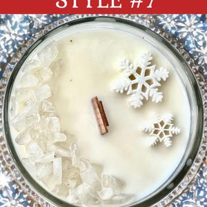 May include: A round candle in a glass container with smooth white wax, a single rectangular wooden wick, a cluster of clear crystal-like stones along one side, and two white snowflake-shaped wax embeds. The text STYLE #7 is visible.