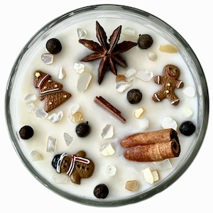 May include: A clear glass candle filled with white wax, decorated with gingerbread men, a Christmas tree, star anise, cinnamon sticks, and peppercorns. The candle is a festive holiday decoration.