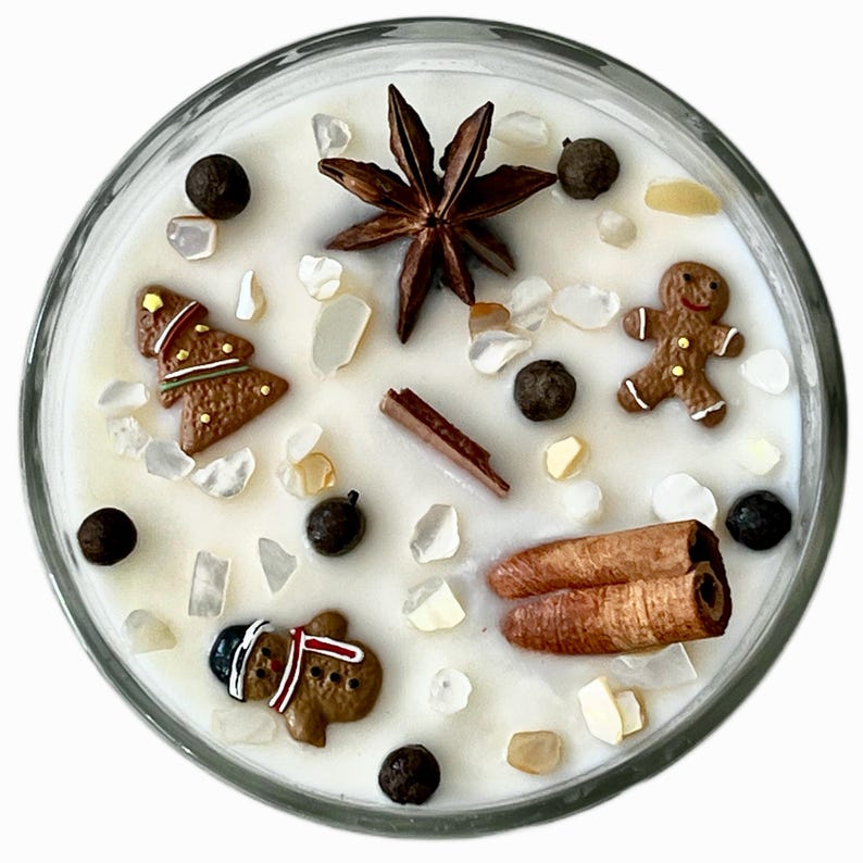 May include: A clear glass candle filled with white wax, decorated with gingerbread men, a Christmas tree, star anise, cinnamon sticks, and peppercorns. The candle is a festive holiday decoration.