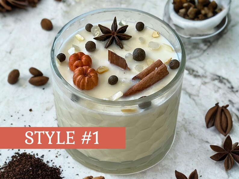 May include: A clear glass candle with a creamy wax interior, decorated with miniature orange pumpkins, star anise, cinnamon sticks, and peppercorns. The candle is labeled "STYLE #1" on a red banner.