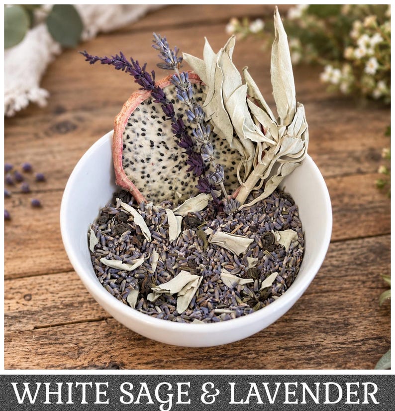 May include: A white ceramic bowl filled with a mixture of dried lavender buds, green tea leaves, and white sage pieces. A slice of dried dragon fruit, a sprig of purple lavender, and several white sage leaves are arranged upright in the bowl.
