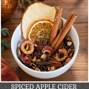 May include: A white bowl filled with a mixture of dried ingredients including cinnamon sticks, star anise, dried orange slices, and dried apple slices. The text "SPICED APPLE CIDER" is printed in white capital letters at the bottom of the image.