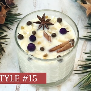 May include: A clear glass candle container with a honeycomb texture, filled with white wax. The top is decorated with a star anise, two cinnamon sticks, small purple spheres, dark peppercorns, and light-colored stone chips. Text reads STYLE #15.