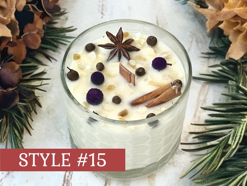 May include: A clear glass candle container with a honeycomb texture, filled with white wax. The top is decorated with a star anise, two cinnamon sticks, small purple spheres, dark peppercorns, and light-colored stone chips. Text reads STYLE #15.