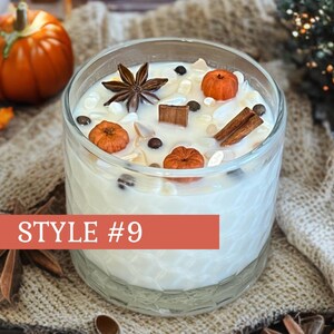 May include: A clear glass candle filled with white wax, decorated with miniature orange pumpkins, star anise, and cinnamon sticks. The candle is labeled "STYLE #9" in a red banner. A small pumpkin and fall leaves are in the background.
