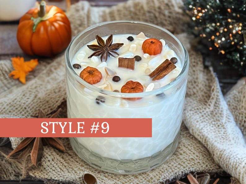 May include: A clear glass candle filled with white wax, decorated with miniature orange pumpkins, star anise, and cinnamon sticks. The candle is labeled "STYLE #9" in a red banner. A small pumpkin and fall leaves are in the background.
