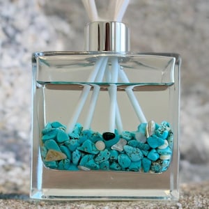 May include: A clear, square glass diffuser bottle filled with turquoise stones and white reeds. The bottle has a silver cap and is filled with a clear liquid. The reeds are arranged to disperse the fragrance.