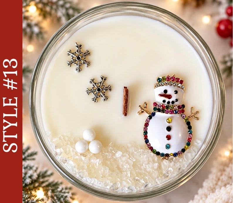 May include: A round glass candle container filled with white wax, featuring a wooden wick, two silver-toned snowflake charms, three small white spheres, and a snowman-shaped brooch decorated with colorful rhinestones. Text reads STYLE #13.