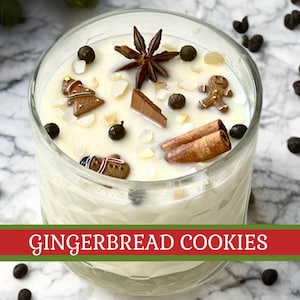 May include: A clear glass candle filled with a creamy white wax, decorated with gingerbread cookie shapes, star anise, and cinnamon sticks. The candle has the text "GINGERBREAD COOKIES" in a red and green banner.