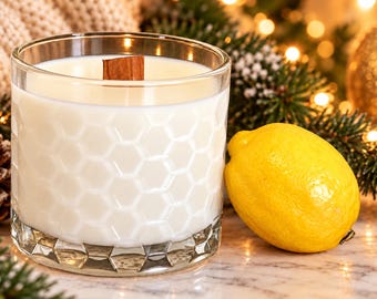 May include: A white candle in a clear glass jar with a textured honeycomb pattern on the sides and a wooden wick. A single bright yellow lemon sits next to the glass jar. The candle wax is smooth and opaque, filling the glass container.
