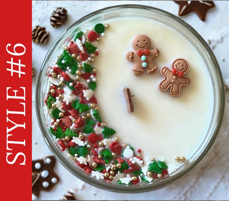 May include: A round glass candle container filled with white wax and a wooden wick. The surface is decorated with a crescent-shaped arrangement of red, green, and white holiday-themed sprinkles and gold beads, alongside two small gingerbread man figures.