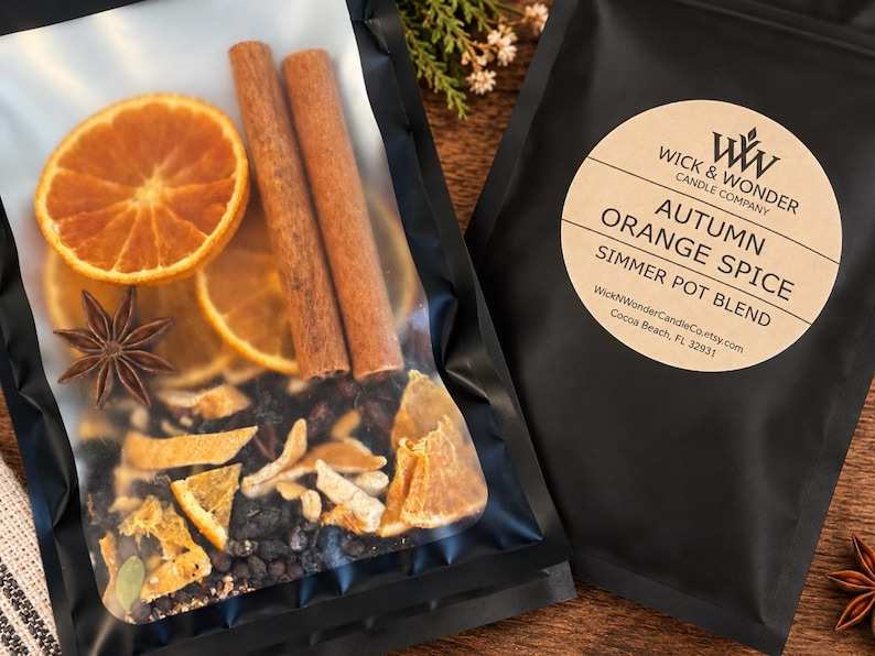 May include: A black pouch containing a simmer pot blend of dried orange slices, two cinnamon sticks, and a star anise. The label reads WICK & WONDER CANDLE COMPANY, AUTUMN ORANGE SPICE, SIMMER POT BLEND, and includes the website and location address.