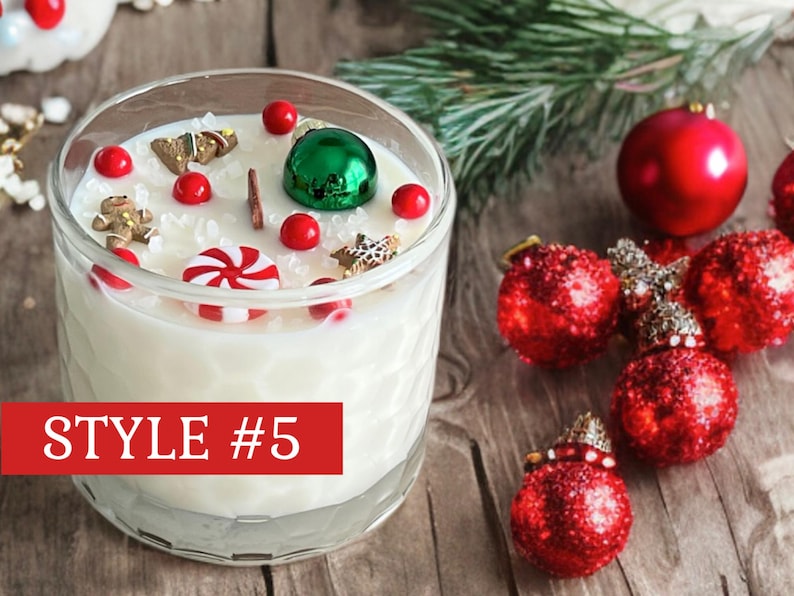 May include: A clear glass candle with a textured honeycomb pattern filled with white wax, topped with miniature gingerbread figures, a red and white peppermint candy, red spheres, and a green ornament. A red rectangular label reads STYLE #5.