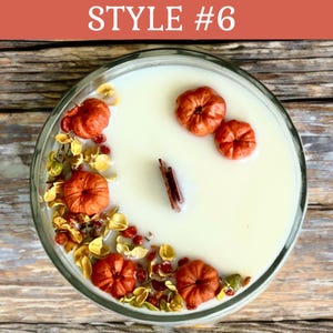 May include: A clear glass candle with a creamy white wax, decorated with small orange pumpkins, dried flowers, and a cinnamon stick. The text "STYLE #6" is displayed in white on an orange background.