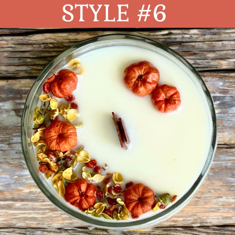 May include: A clear glass candle with a creamy white wax, decorated with small orange pumpkins, dried flowers, and a cinnamon stick. The text "STYLE #6" is displayed in white on an orange background.