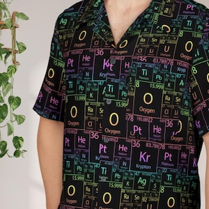 May include: Black button-up shirt featuring a colorful periodic table design. The shirt displays various chemical elements and their symbols, including Oxygen, Platinum, and Krypton. The short-sleeved shirt has a classic collar.