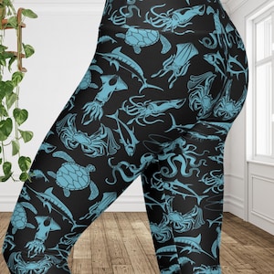 Op de afbeelding: Zwarte legging met een herhaald patroon van lichtblauwe zeedieren, waaronder schildpadden, inktvissen, krabben en vissen. De legging heeft een hoge taille en is gemaakt van een rekbaar materiaal.