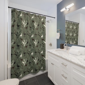 May include: A green shower curtain with a repeating pattern of deer silhouettes, crosshairs, and antlers. The deer are in white, brown, and black, set against a muted green background. The curtain is hanging in a bathroom setting.