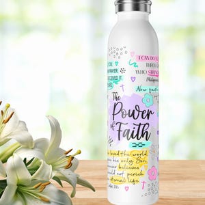 Puede incluir: Botella de agua blanca de acero inoxidable con tapa plateada, decorada con las palabras "The Power of Faith" y otras frases inspiradoras en varios colores. Un ramo de lirios blancos está en primer plano.