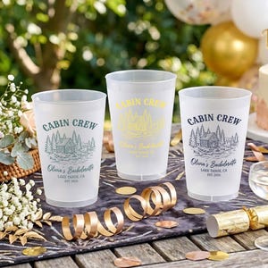 May include: Three frosted plastic cups featuring a cabin illustration, the text "CABIN CREW", "Olivia's Bachelorette", "LAKE TAHOE, CA", and "EST. 2026". The cups are printed in green, yellow, and dark blue ink respectively.