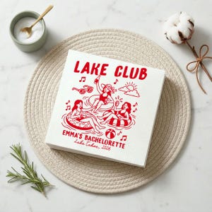 Puede incluir: Una servilleta de papel cuadrada blanca con un estampado gráfico rojo de tres personas en flotadores sobre el agua. El texto dice LAKE CLUB, EMMA'S BACHELORETTE y Lake Tahoe, 2026. El diseño incluye gafas de sol, notas musicales, una pelota de playa y un sol.
