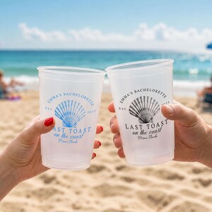 May include: Two translucent plastic cups featuring a seashell graphic and the text "EMMA'S BACHELORETTE EST. 2025 LAST TOAST on the coast Miami, Florida". One cup has blue ink, and the other has black ink, both displaying identical printed designs.