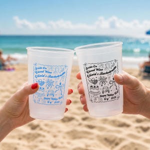 Könnte beinhalten: Zwei durchscheinende Kunststoffbecher mit einem Aufdruck, der den Text "Bride On Cloud Wine Olivia's Bachelorette Napa Valley, CA 2025" sowie Illustrationen von Torte, Auto, Ringkästchen und Schleifen zeigt. Ein Becher hat blaue, der andere schwarze Tinte.