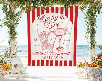 May include: A white and red striped banner with the text "Lucky in Love" and "Olivia's Bachelorette LAS VEGAS, NV". The banner features illustrations of playing cards, dice, and a margarita.