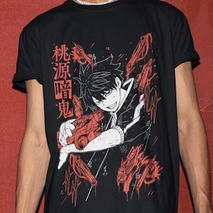 Könnte beinhalten: Schwarzes T-Shirt mit einer rot-weißen Anime-Grafik. Die Grafik zeigt eine Figur, die ein rotes Objekt hält, mit japanischem Text auf der linken Seite. Das Design ist vor einem schwarzen Hintergrund.