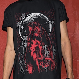 May include: Black t-shirt featuring a red illustration of a demonic figure against a white moon. The graphic design includes stylized text elements. The shirt is a crew neck style.