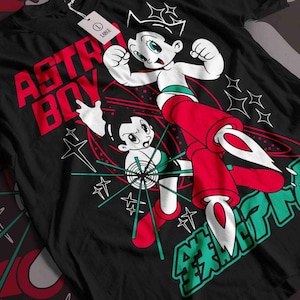 May include: Black t-shirt with a colourful Astro Boy graphic. The design includes the words "ASTRO BOY" in red, and Japanese text in green. The image features Astro Boy in a dynamic pose with white and red accents. A tag is visible.