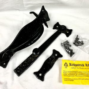 May include: Black cast iron gate hardware set, including a latch, hinges, and a strike plate. The set includes screws and a yellow leaflet with text. The hardware is designed for gates and doors.