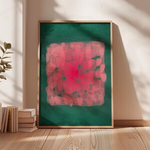 May include: A framed abstract art print. The artwork features a central, vibrant pink shape surrounded by a softer pink pattern, set against a deep green background. The frame is a natural wood tone, adding warmth to the piece.
