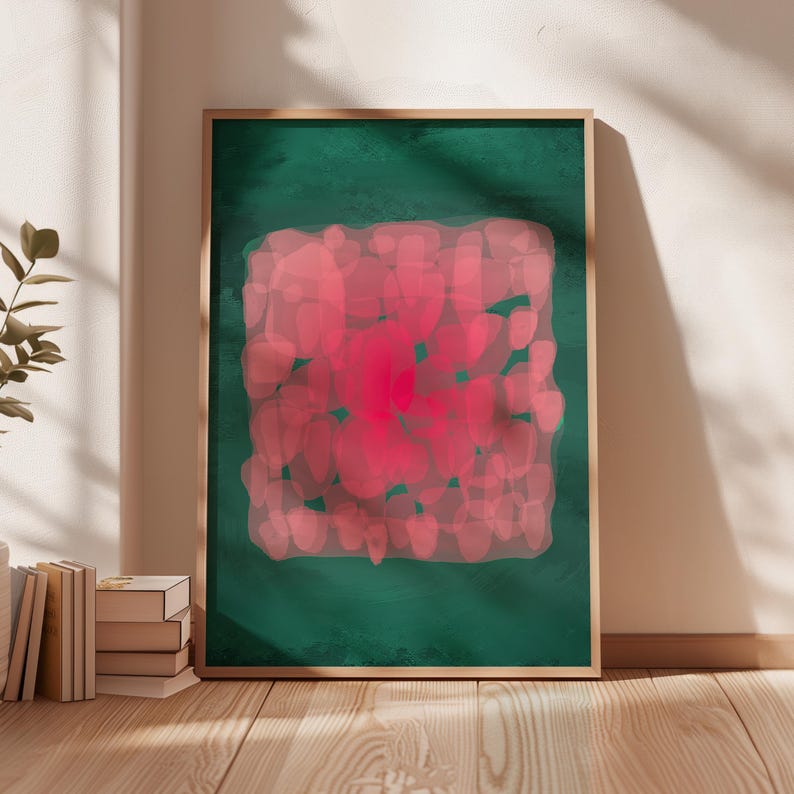May include: A framed abstract art print. The artwork features a central, vibrant pink shape surrounded by a softer pink pattern, set against a deep green background. The frame is a natural wood tone, adding warmth to the piece.