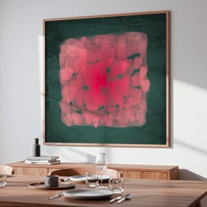 May include: A framed abstract art piece with a dark green background and a central design of overlapping pink shapes. The artwork is displayed above a wooden dining table set with plates, glasses, and silverware.