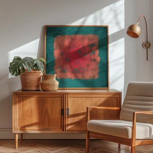 May include: A framed abstract art print with a teal background and a central red and orange design. The artwork hangs above a wooden cabinet with a potted plant and a woven vase. A mid-century modern chair sits nearby.