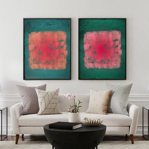 May include: Two framed abstract art prints. Each features a square of red and orange brushstrokes on a teal green background. The artwork hangs above a white sofa with decorative pillows and a black coffee table.