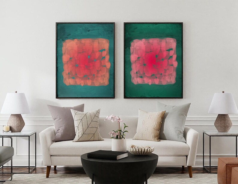 May include: Two framed abstract art prints. Each features a square of red and orange brushstrokes on a teal green background. The artwork hangs above a white sofa with decorative pillows and a black coffee table.