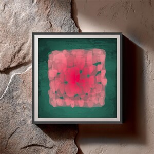 May include: Square framed abstract art print. The artwork features a central cluster of pink shapes on a dark green background. The frame is black with a white border. The artwork is displayed against a textured, light brown stone wall.