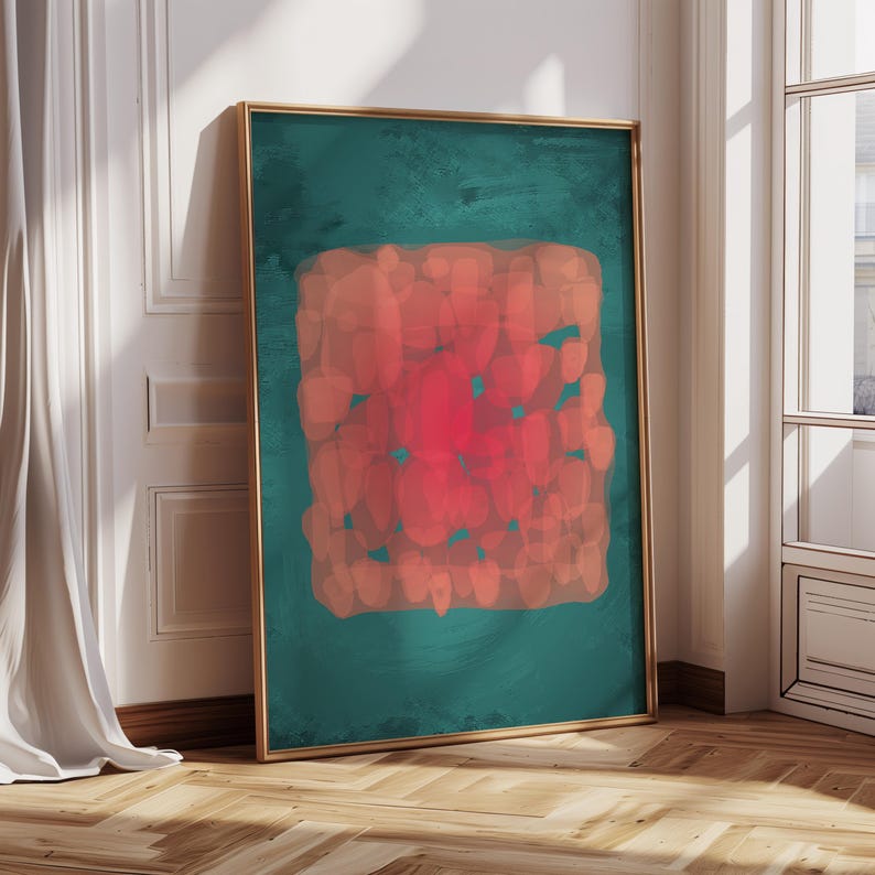 May include: Abstract art print in a gold frame. The artwork features a teal background with a central, textured, rectangular shape in shades of red and orange. The artwork is leaning against a white wall.