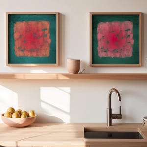May include: Two framed abstract art pieces with a square design in shades of red and orange on a teal background. The artwork hangs above a wooden shelf with a ceramic cup and a stack of white bowls. A wooden countertop features a sink and a bowl of yellow fruit.