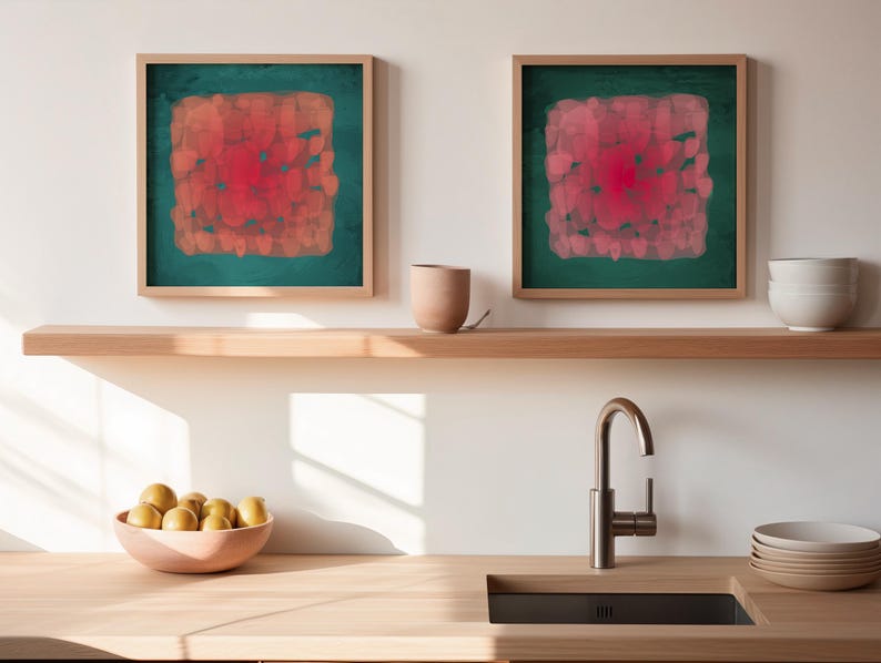 May include: Two framed abstract art pieces with a square design in shades of red and orange on a teal background. The artwork hangs above a wooden shelf with a ceramic cup and a stack of white bowls. A wooden countertop features a sink and a bowl of yellow fruit.