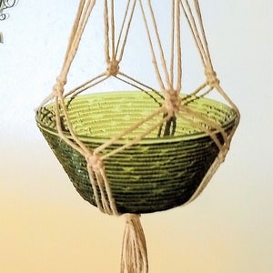 May include: A macrame plant hanger with a green glass bowl. The hanger is made of natural twine and has wooden beads. The bowl is suspended from the hanger by the twine.